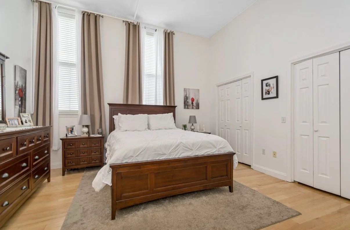 Furnished bedroom with tall windows and closets, shown as an example apartment at Foster Place
