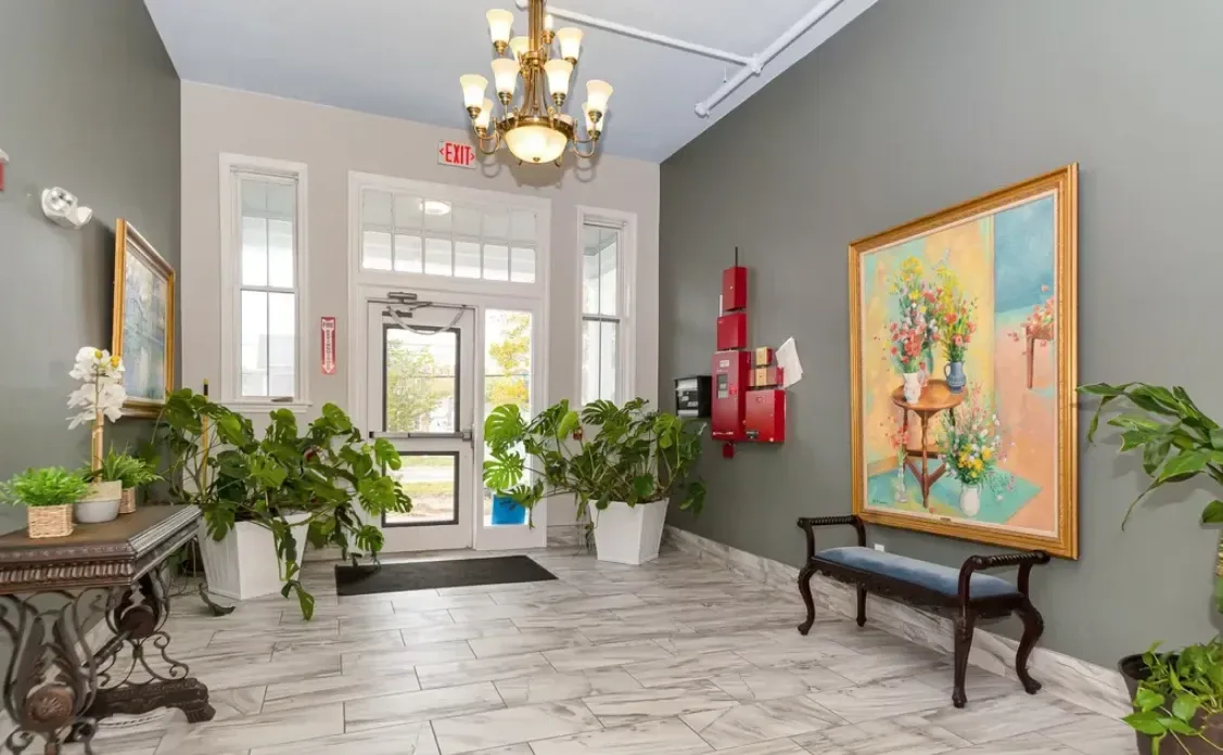 The front lobby of the main building at Foster Place, with a chandelier, artwork, a bench and plants by the glass entrance door